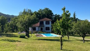 Une maison à deux étages avec une piscine, entourée d’une pelouse verdoyante et d’arbres.