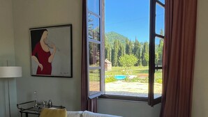 Un salon avec un canapé blanc, un tableau au mur, une table avec des verres et une fenêtre donnant sur un paysage verdoyant.