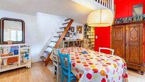 A dining area with a table covered in a polka dot tablecloth, wooden chairs, and a staircase leading to an upper level. - GuestReady - loft with workspace and music (Paris 19 Buttes-Chaumont)