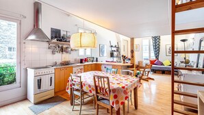 A modern kitchen with a central island, wooden cabinets, and a large window. - GuestReady - loft with workspace and music (Paris 19 Buttes-Chaumont)