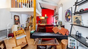 A loft-style living space with a high ceiling, a staircase, and a red accent wall. - GuestReady - loft with workspace and music (Paris 19 Buttes-Chaumont)