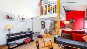 A spacious living room with a piano, a dining area, and a red accent wall. - GuestReady - loft with workspace and music (Paris 19 Buttes-Chaumont)