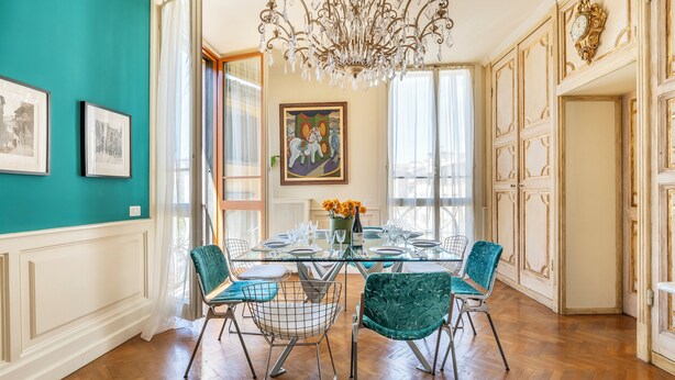 Et spiseområde med et glasbord, teal stole og en lysekrone.