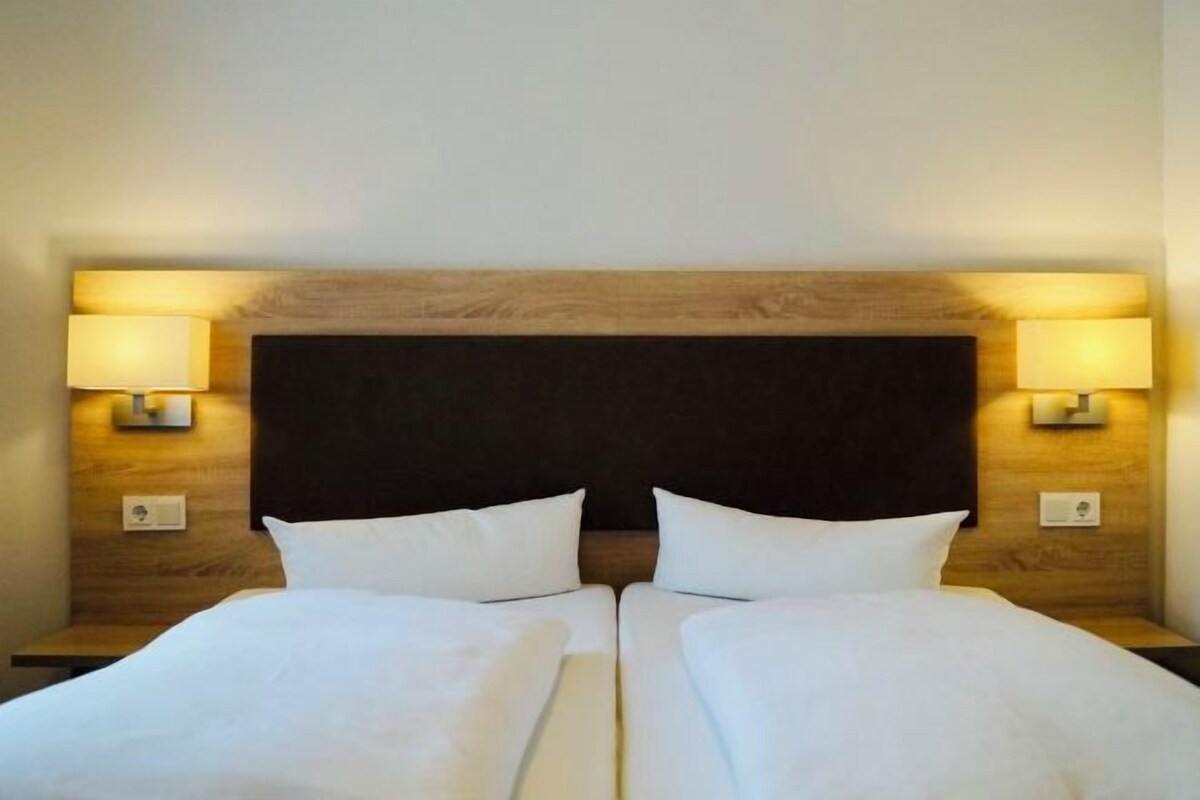 A double bed with two pillows, a wooden headboard, and two bedside lamps.
