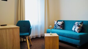 A room with a teal sofa, a wooden side table with a vase, a blue chair, and a wooden desk. - Hotel & Restaurant Pelikan (Beuron)
