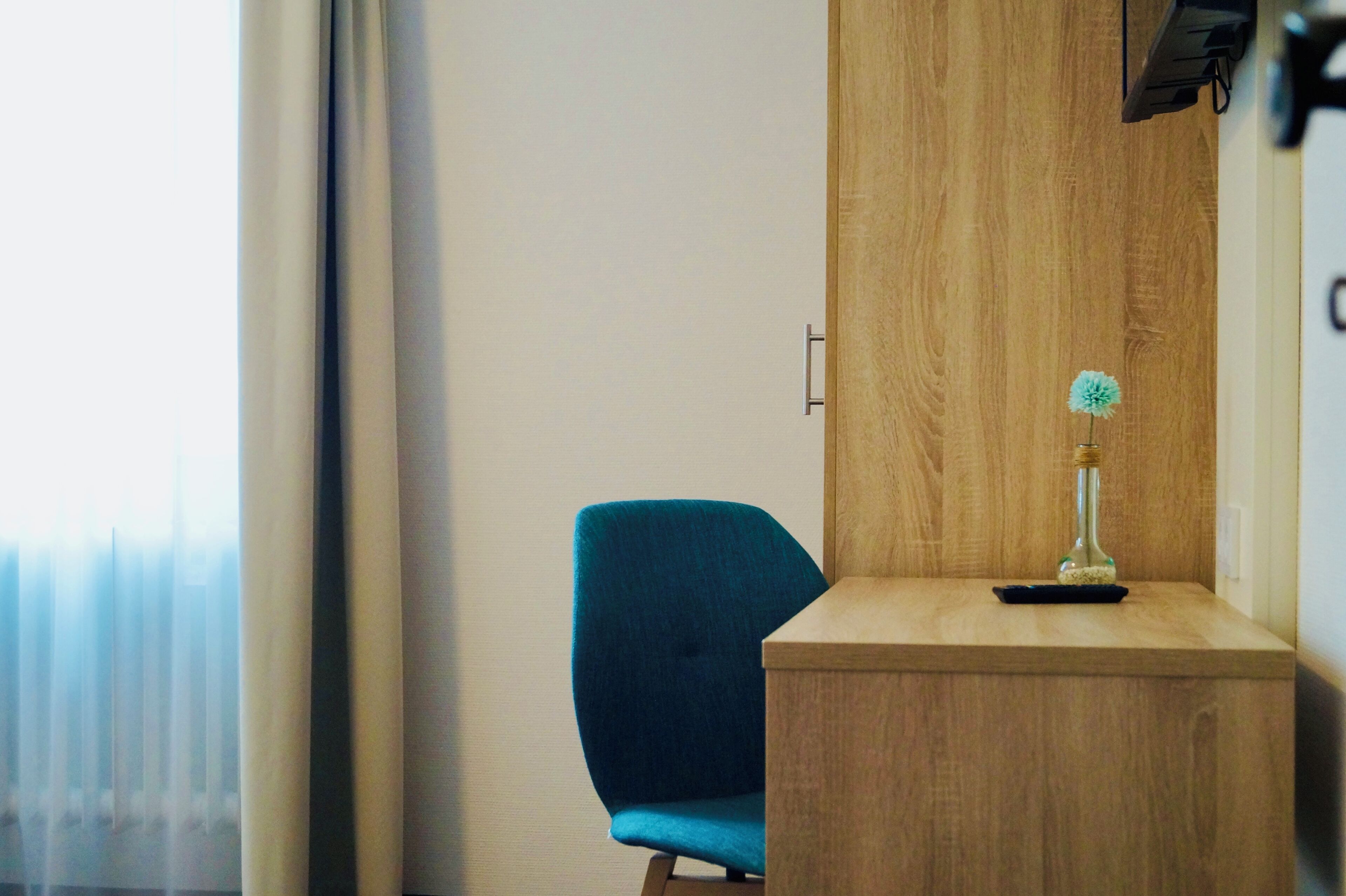A hotel room with a wooden cabinet, a blue chair, and a small table with a decorative item.