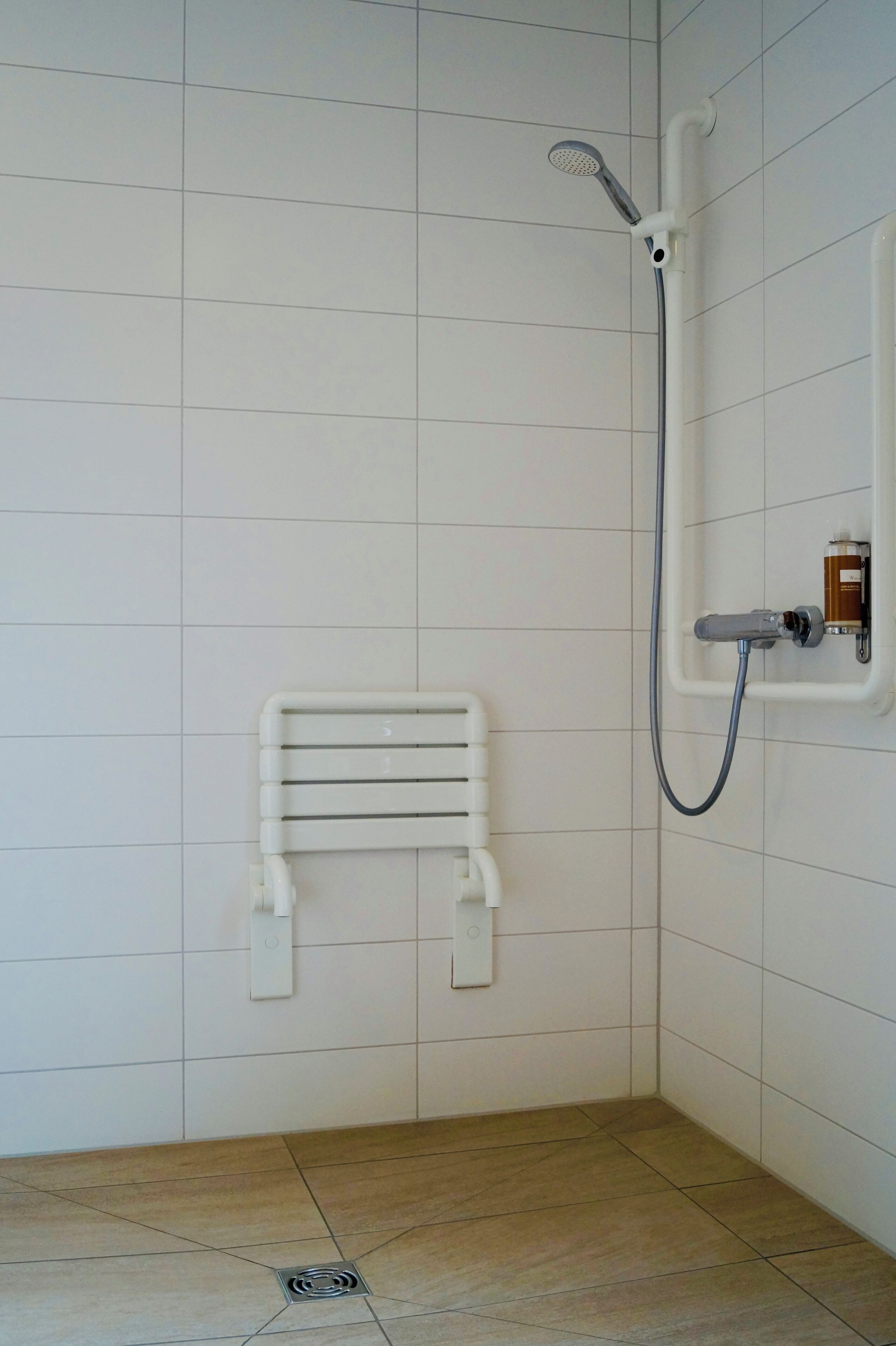 Un petit espace de douche carrelé, équipé d’un pommeau de douche à main et d’un robinet fixé au mur.