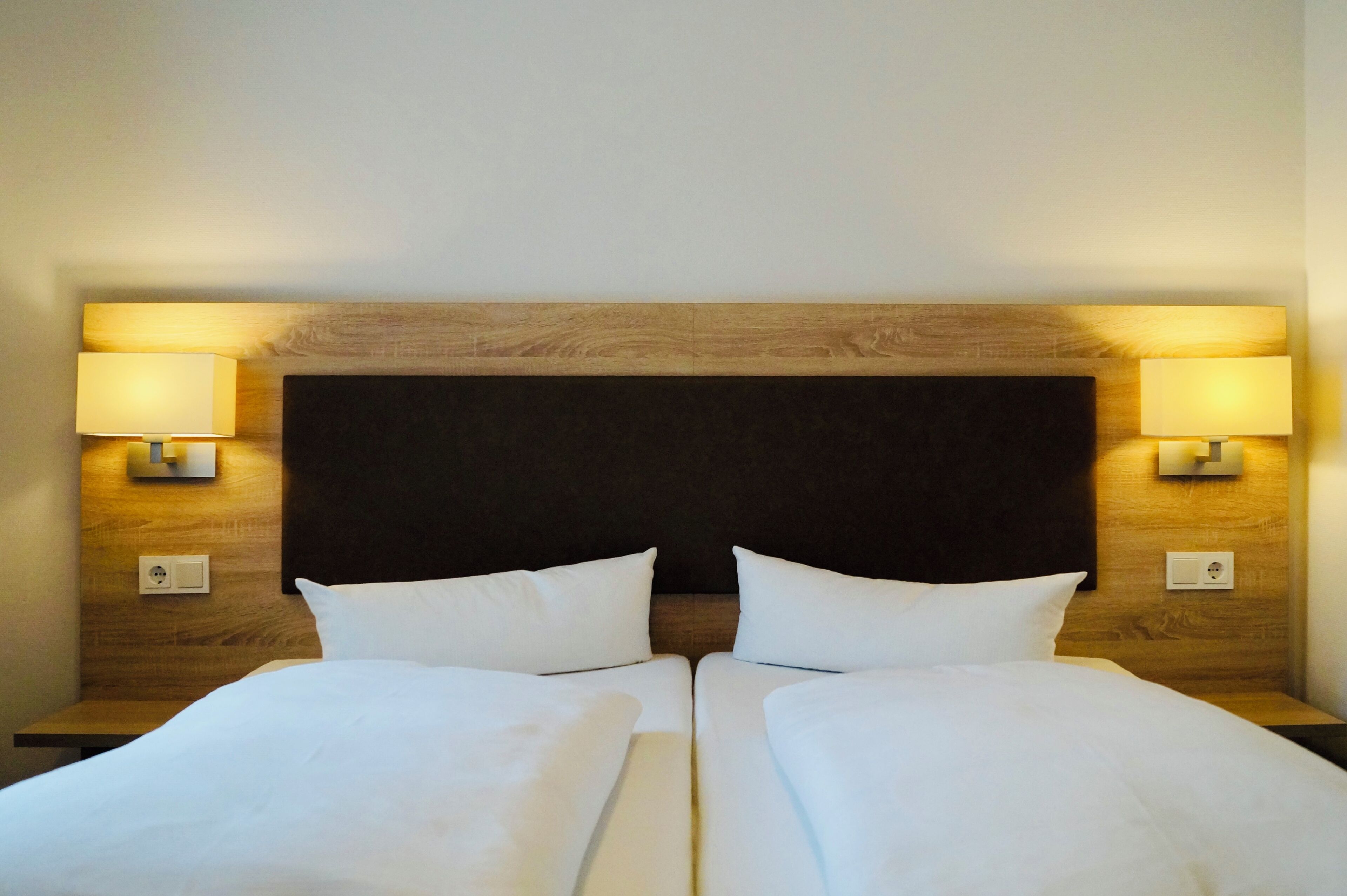 Ein Doppelbett mit Holz Kopfteil, zwei Nachttischlampen und einem Lichtschalter an der Wand.