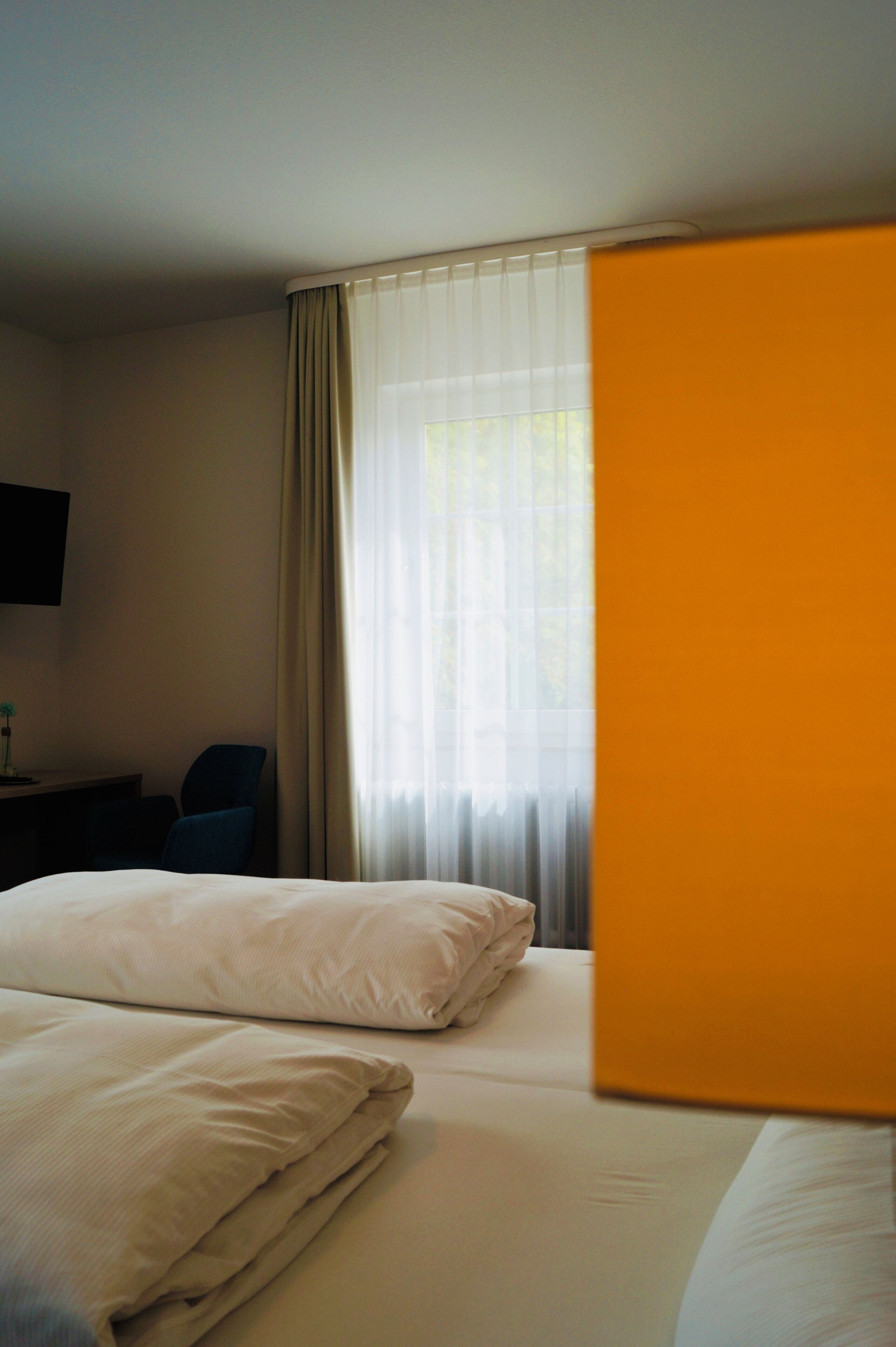 A hotel room with two beds, a television on the wall, and a window with curtains.