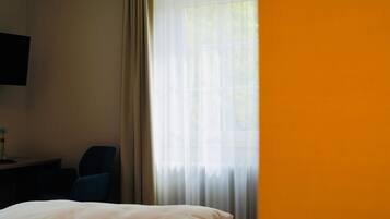 A hotel room with two beds, a television on the wall, and a window with curtains.