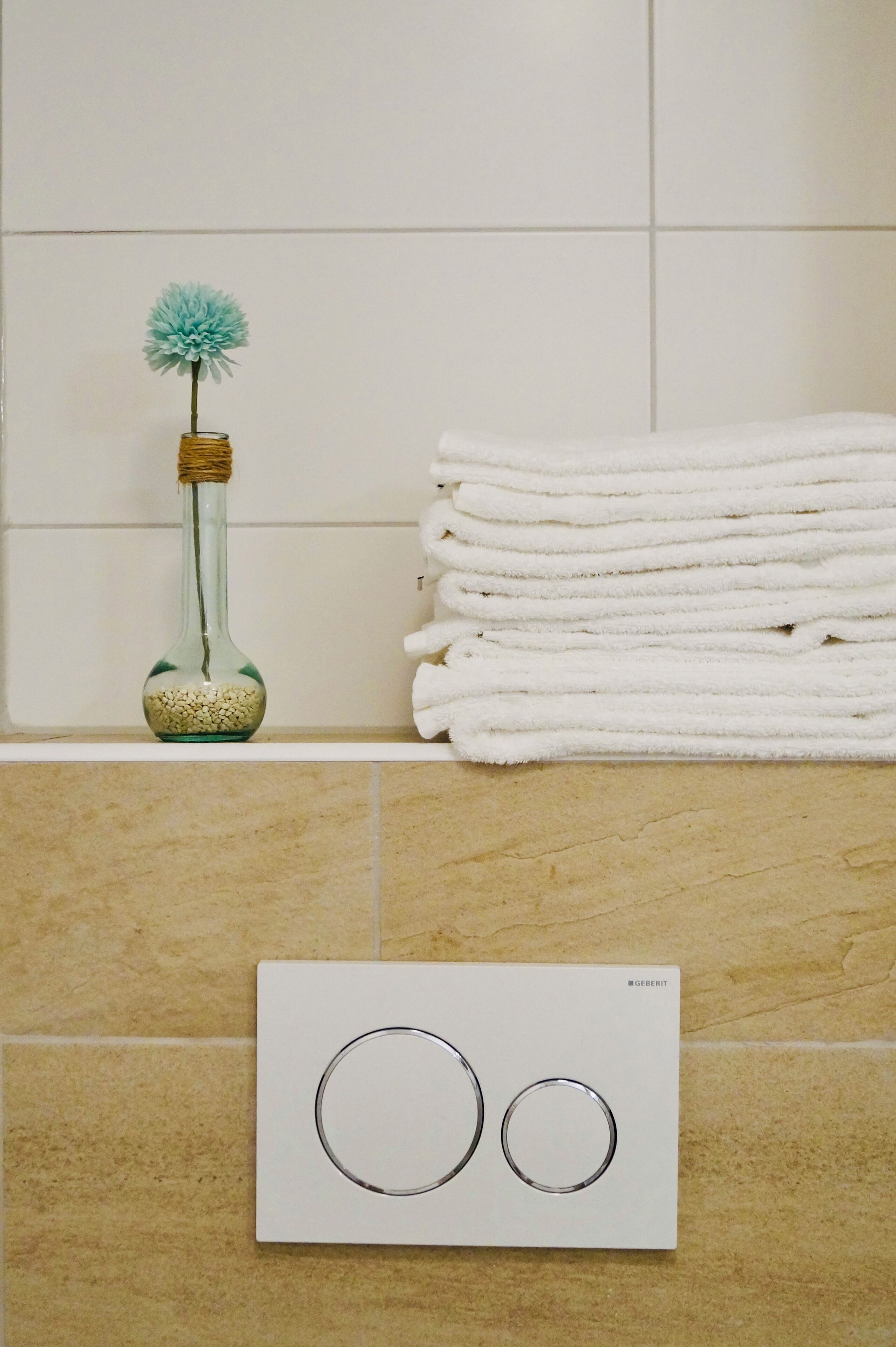 A bathroom with a towel stack, a decorative bottle, and a thermostat control panel.
