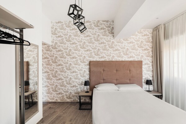 Una habitación de hotel moderna con una cama grande, dos mesitas de noche con lámparas, un colgador de techo y papel tapiz estampado.
