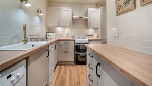 Een moderne keuken met witte kastjes, een houten aanrecht, een ingebouwde oven en een vaatwasser.