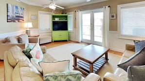 A living room with a green entertainment unit, a beige sofa, a wooden coffee table, and a ceiling fan.