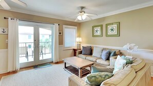 A living room with a beige sofa, a coffee table, a ceiling fan, and a view through the sliding glass door.