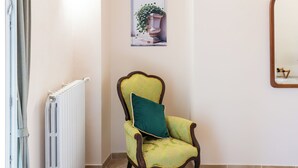 A room with a radiator, a chair with a green cushion, a framed picture on the wall, and a mirror.