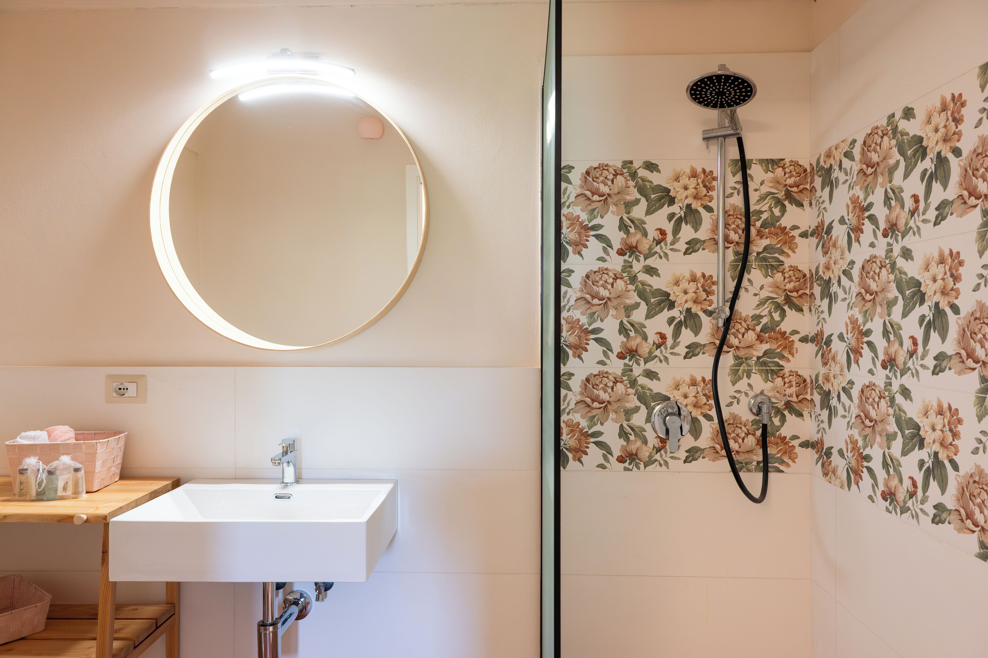 A bathroom with a round mirror, a sink, and a shower with floral tiles.