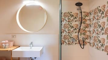 Ein Badezimmer mit rundem Spiegel, Waschbecken und Dusche mit floralen Fliesen.