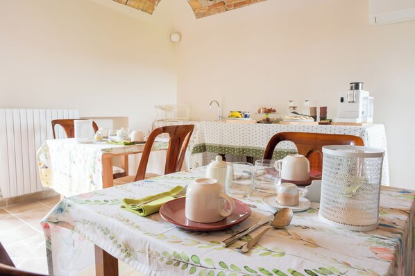 A dining area with a table set for two, featuring a coffee maker, teapot, cups, and a basket. - ACERO ROSSO (Moncalvo)