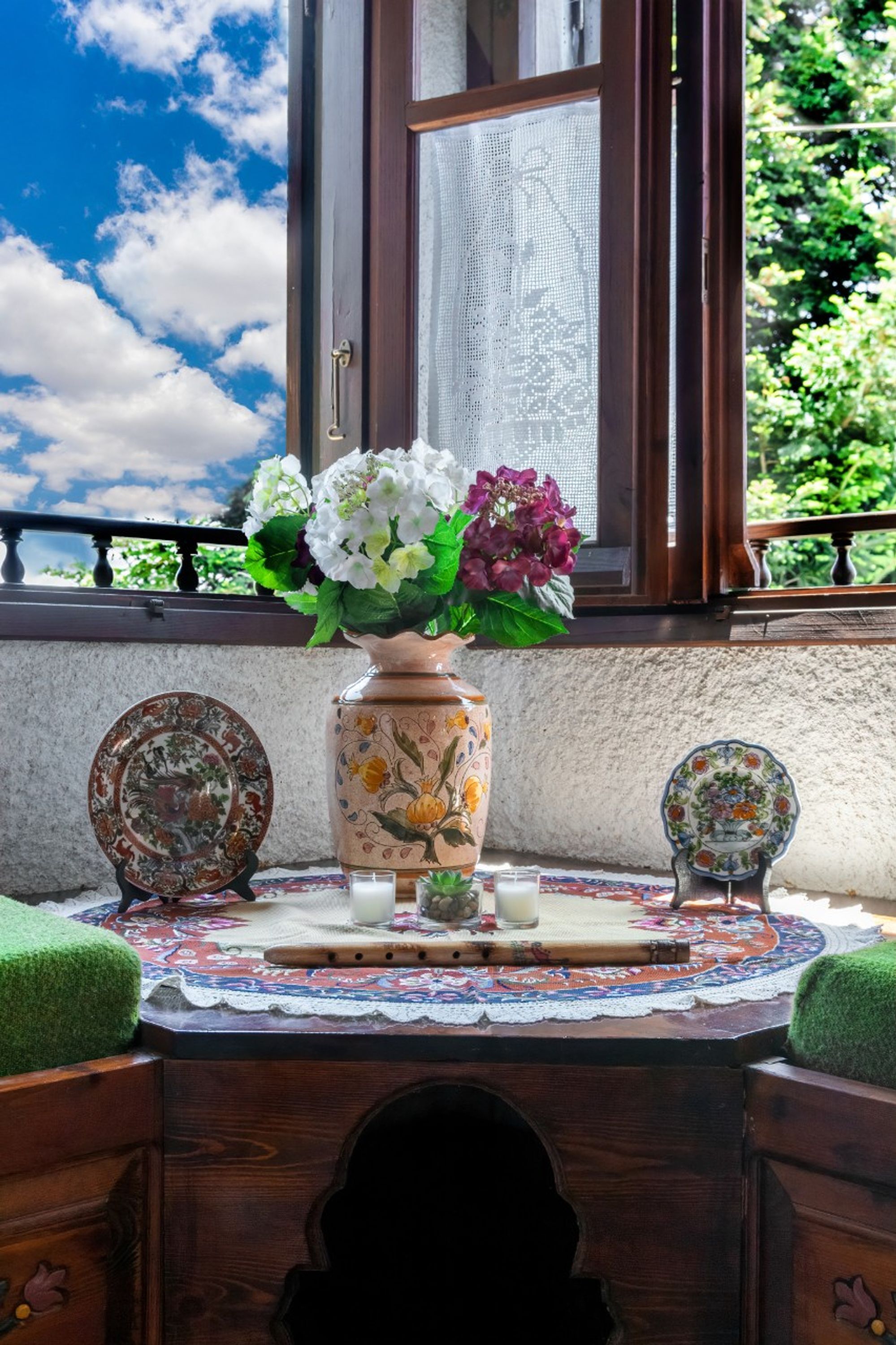 A wooden table with a lace tablecloth, a vase with flowers, and two decorative plates.