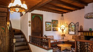 Un escalier en bois avec une rampe, une porte en bois surmontée d’un arc vert, et un coin salon avec une table et des chaises.