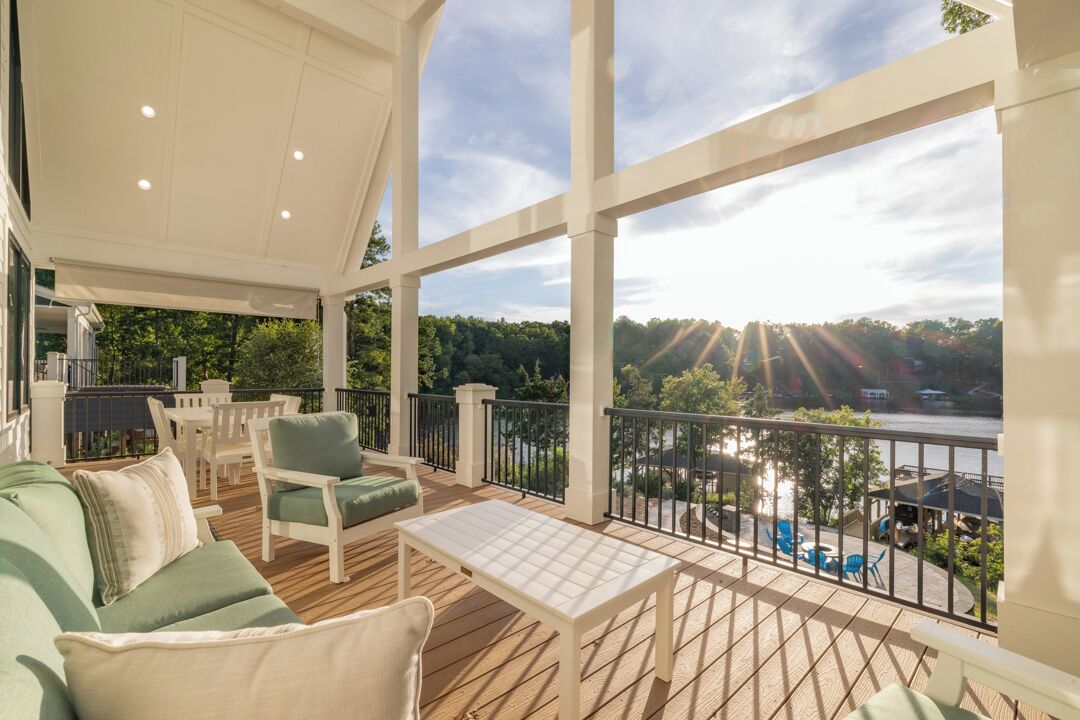 A covered outdoor deck with seating, a table, and a view of a river and trees.