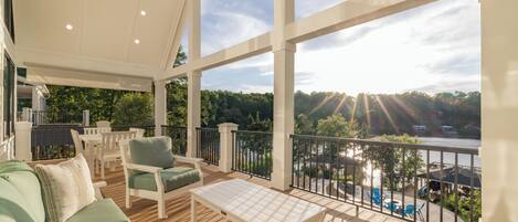 A covered outdoor deck with seating, a table, and a view of a river and trees.