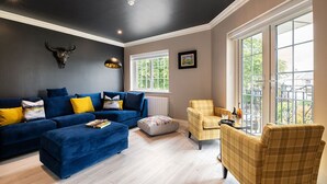 A living room with a dark ceiling, a blue sofa set, a yellow armchair, and a large window with a view of trees. - Killarney Centre Home comprising 4 separate Apartments (Sleeps 18) (Killarney)