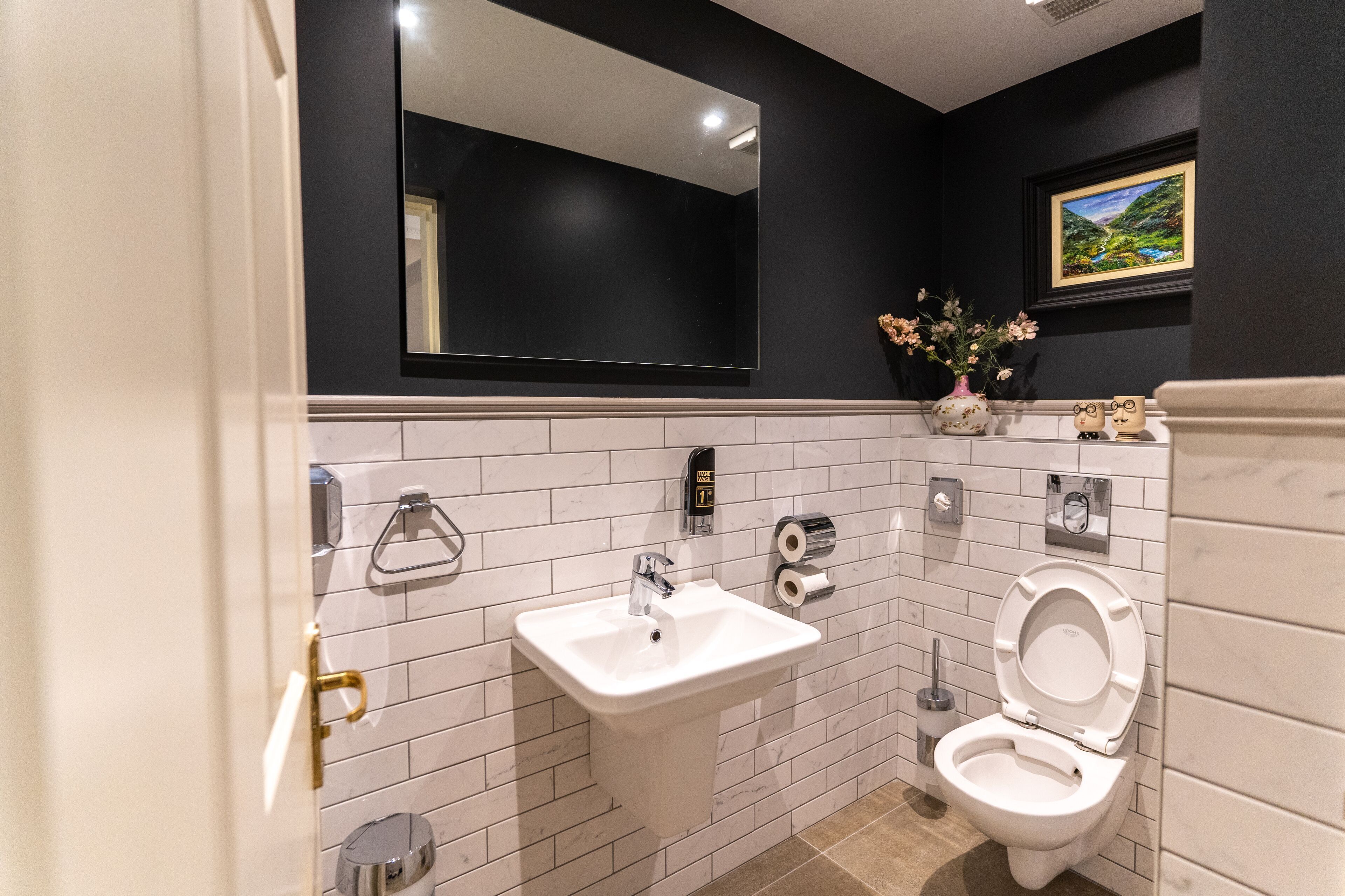 A bathroom with a white sink, a toilet, a mirror, and a framed picture on the wall.
