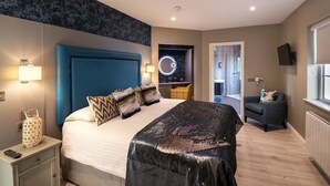 A modern hotel room with a large bed, a blue headboard, a circular wall decoration, a small armchair, and a television. - Killarney Centre Home comprising 4 separate Apartments (Sleeps 18) (Killarney)