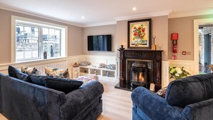 A living room with a fireplace, a television mounted on the wall, and a large window with a city view. - Killarney Centre Home comprising 4 separate Apartments (Sleeps 18) (Killarney)