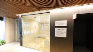 A modern building entrance with a glass door, a sign indicating swimming pool rules, and a wooden ceiling.