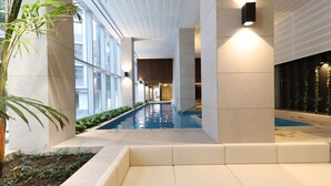 A modern indoor pool area with a long view corridor, large windows, and a seating area with a plant.