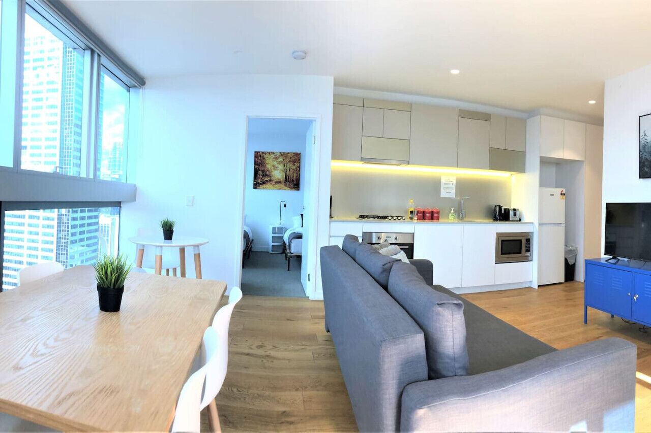 Un apartamento moderno con comedor, sala de estar con sofá, cocina con gabinetes blancos y televisor sobre un mueble azul.