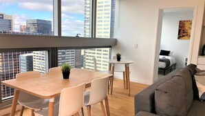 A modern living room with a grey sofa, a wooden dining table with chairs, and a small round table with a plant.