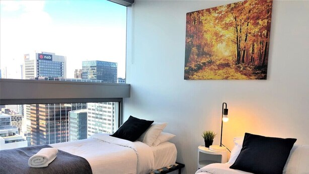 A hotel room with two beds, a city view, a painting on the wall, and a bedside lamp.