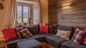 A cozy living room with a sectional sofa, a wooden wall, and a window with curtains. - Casa dell'Alpinista in Cortina d'Ampezzo (Cortina d´Ampezzo)
