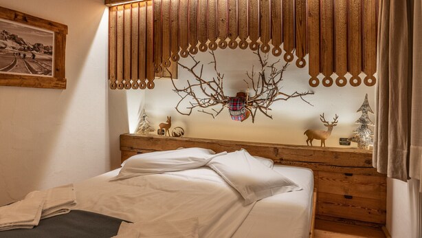 A bedroom with a wooden headboard, a bed with white linens, and a wall-mounted decoration of a tree with antlers. - Casa dell'Alpinista in Cortina d'Ampezzo (Cortina d´Ampezzo)