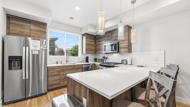 A modern kitchen with a stainless steel refrigerator, a microwave, wooden cabinets, a large island, and pendant lighting. - 2BD w/ Rooftop • Minutes to LoHi & Sloan’s Lake (Denver)