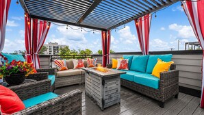 A covered outdoor seating area with wicker furniture, a fire pit, and red and white striped curtains. - 2BD w/ Rooftop • Minutes to LoHi & Sloan’s Lake (Denver)