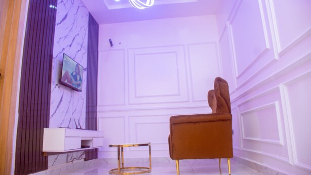 A modern living room with a marble wall, a brown armchair, a white console table, and a gold-framed side table. - Lekki Aprt/pool/gym/sleeps 6/ Freep/tv/wifi (Lekki)