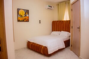 Un dormitorio con cama, un cuadro en la pared, un equipo de aire acondicionado y una puerta.