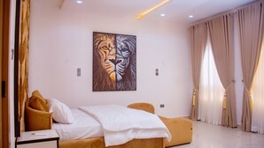 A modern bedroom with a bed, a bedside table, a large painting of a lion's face, and beige curtains. - Lekki Aprt/pool/gym/sleeps 6/ Freep/tv/wifi (Lekki)