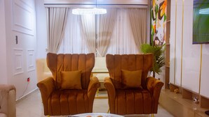 A modern living room with two brown armchairs, a marble coffee table, and a television on the wall. - Lekki Aprt/pool/gym/sleeps 6/ Freep/tv/wifi (Lekki)