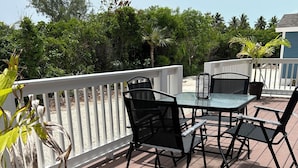 A wooden deck with a table and chairs, surrounded by a white railing and greenery.