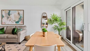 A modern living room with a wooden dining table, a sofa with green cushions, a large abstract painting, a mirror, and a sliding glass door leading to a balcony. - Marie's Oceanfront Condo-1bdrm-3 Pools

 (St. Thomas)