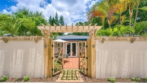 Een houten pergola leidt naar een perceel met een verhard terras en een uitzicht op weelderige begroeiing.