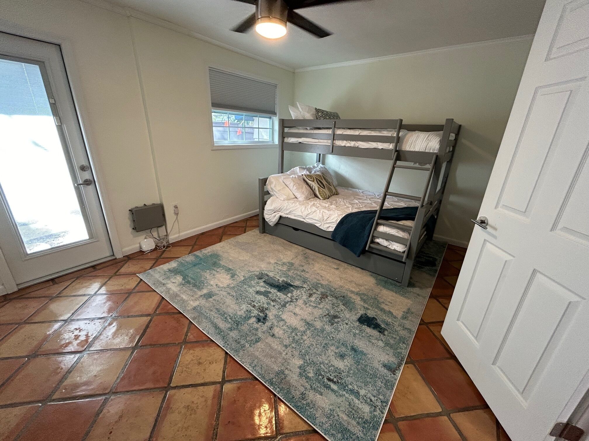 A room with a bunk bed, a large rug, a window with blinds, and a door.