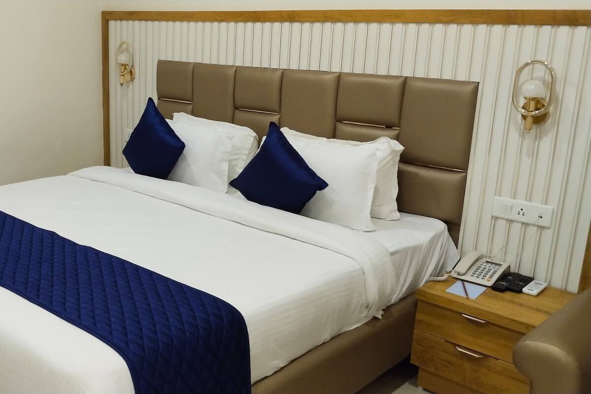 Une chambre d’hôtel avec un grand lit, une table de chevet en bois avec un téléphone et un luminaire fixé au mur.