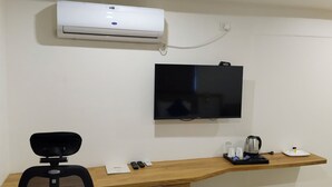 Une chambre d’hôtel équipée d’un climatiseur mural, d’un téléviseur à écran plat, d’un bureau avec une chaise et d’un plateau avec une bouilloire et des tasses.